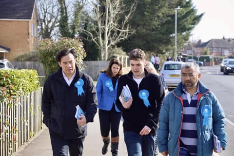 Jackson walking with campaigners wearing blue rosettes along a residential road