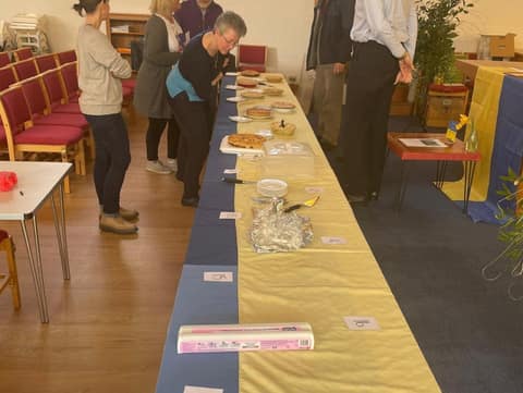 Long table of apple pies in blue and yellow, volunteers looking on