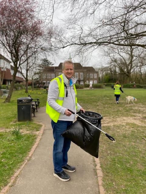 Volunteer in hi-vis with a litter picker on a path across the green