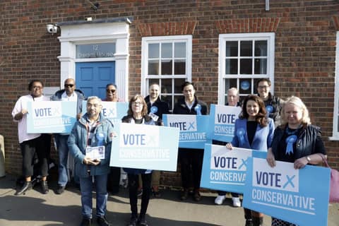 Conservative volunteers holding Vote Conservative boards outside a brick house