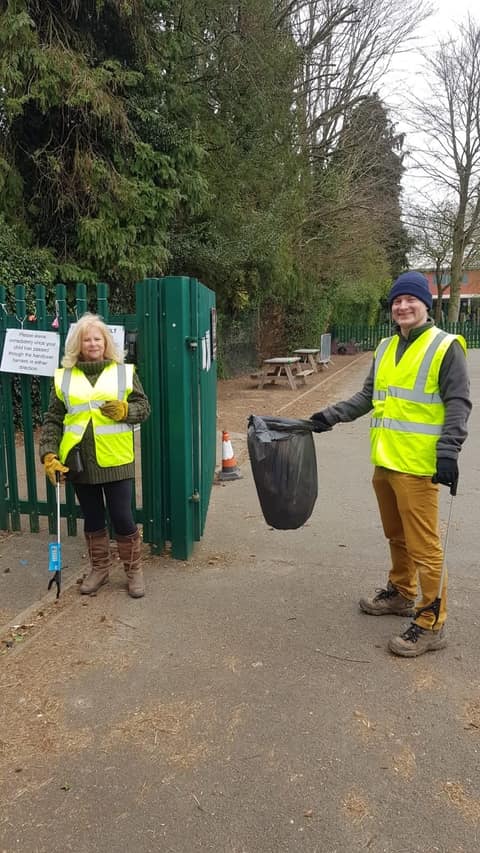 Two litter pickers in hi-vis by a park gate