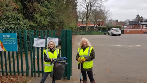 Two volunteers in hi-vis with a full bag by a car park