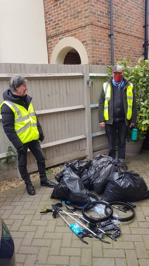 Litter pickers with bags of rubbish by a house